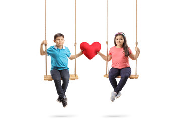 Little boy and a little girl on a swing holding a red heart and looking at the camera