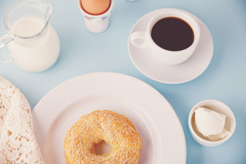 Fresh healthy bagel on a white plate with cup of coffee, cream cheese and eggs for breakfast. Top view.