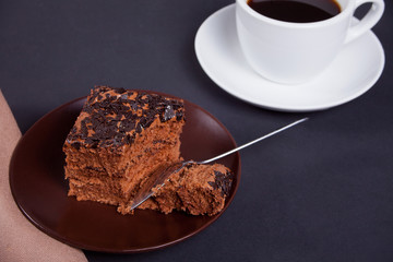 Delicious chocolate cake on the brown plate with cup of coffee on the black table