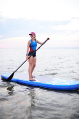 attractive young girl with sup board on the background of the sea and sunset