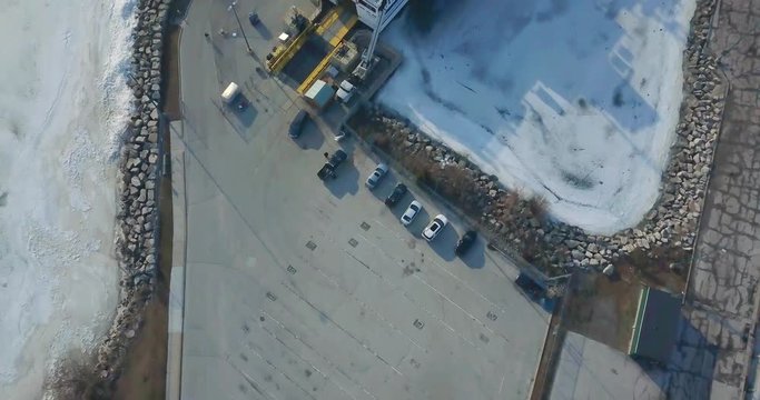Aerial drone shot starting from a parking lot and rising up, revealing a cargo ship at Lake Erie (one of the Great Lakes of North America). Frozen waters. Upwards pedestal movement.