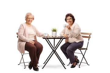 Two elderly women sitting at a table drinking coffee and smiling at the camera