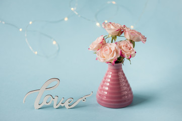 Coral roses on blue background with bokeh and Love word. Postcard concept. Happy Mother's Day, Women's Day or Birthday. Minimalism, selective focus.