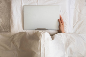 Girl lying with a laptop in bed covered by blanket. Woman can't sleep and have to work late at night. Top view