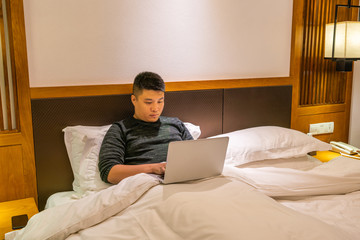 Asian man using laptop on the bed at night