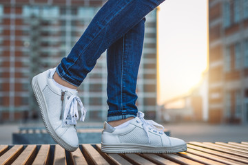 Woman wearing jeans and white sneakers is standing in city after sunset
