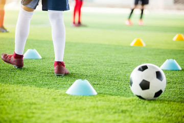 soccer player is jogging with blurry cone markers and football on  artificial turf