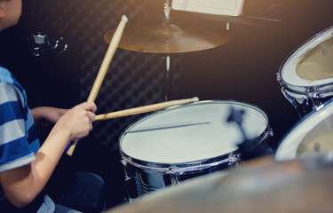 blurry image of wooden drumsticks in hands of Asian kid wearing blue striped t-shirts to learning...