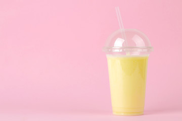 Making a milkshake. plastic disposable glass with a banana milkshake on a bright trendy pink background. space for text