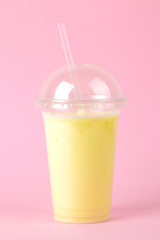 Making a milkshake. plastic disposable glass with a banana milkshake on a bright trendy pink background.