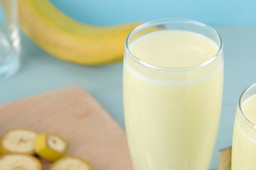 A glass with a banana milkshake and a fresh banana on a blue background. Making a milkshake.