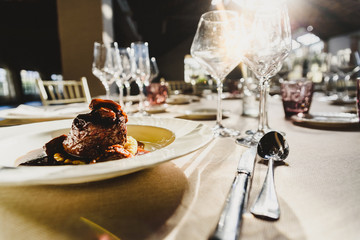 Exquisite veal dish with sauce served in luxury cutlery with sunbeams in a restaurant.