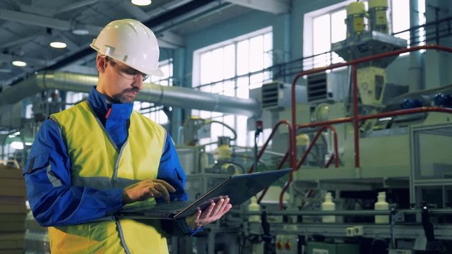 Male specialist is working on a laptop in a facility of a plastic plant