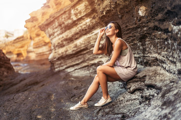Pretty long hair brunette tourist girl relaxing on the stones near sea.