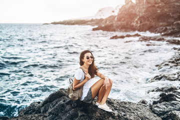Fototapeta na wymiar Pretty long hair tourist girl relaxing on the stones near sea.