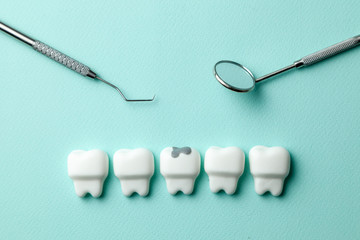 Healthy white teeth and  tooth with caries on green mint background and dentist tools mirror, hook.