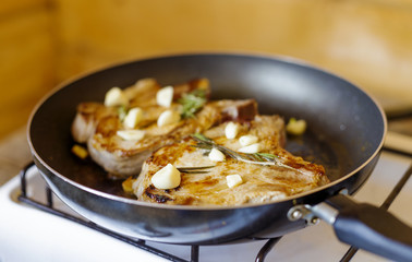 Close up of two roasted pork chops seasoned with garlic and rosemary in black frying pan with selective focus and shallow depth of field