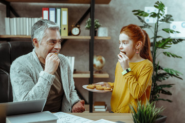 Joyful nice father and daughter eating cookies
