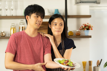 Asian young couple is feeding each other and smiling while cooking salad in kitchen