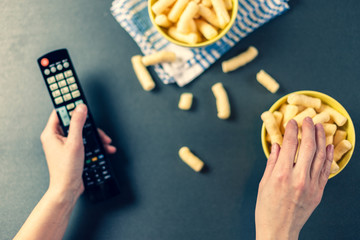 Obraz premium Person with TV remote watching tv and eating chips, romanian pufuleti