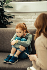 Cheerless unhappy girl putting chin on her knees