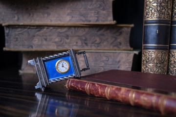 Vintage clock lying on its side on the table on the background of old books.