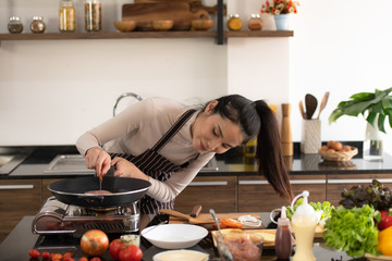 Young woman cooking a hamburger in kitchen with a smile and delicious