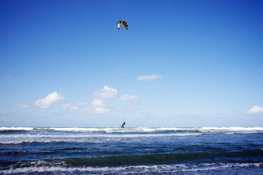 On a beautiful blue sky day a male kitesurfer jumps the wave on his board in Cardiff-by-the-sea, CA.