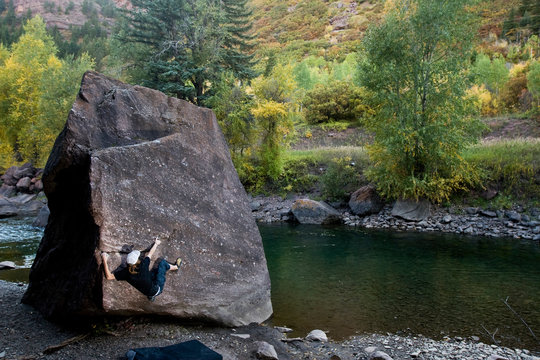A male rock climber working on a bouldering problem next to the Crystal River, in Redstone Colorado.