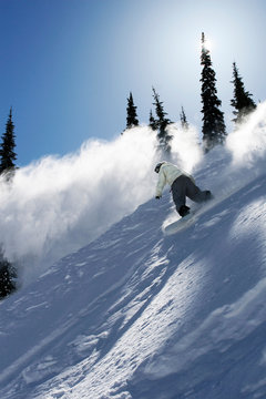 A male snowboarder ripping powder at Schweitzer Mountain Resort, Idaho (back lit).