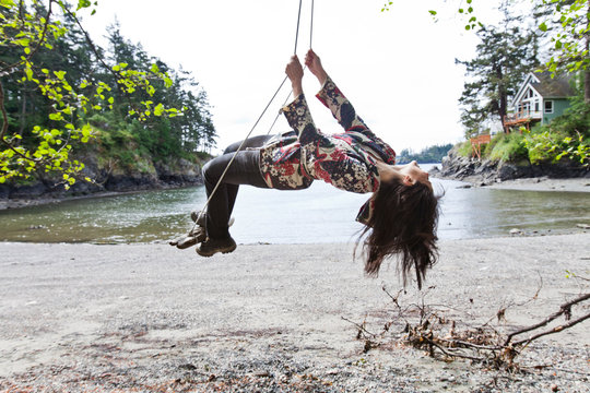 A young woman enjoys a swing hung from a tree near the water's edge of Doe Bay on Orcas Island.