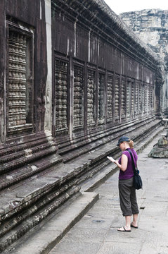 Side view of a woman traveller reading a guidebook at Angkor Wat, Cambodia, on the 6 November 2010. Angkor Wat is a UNESCO World Heritage Site and a major tourist attraction in Cambodia.