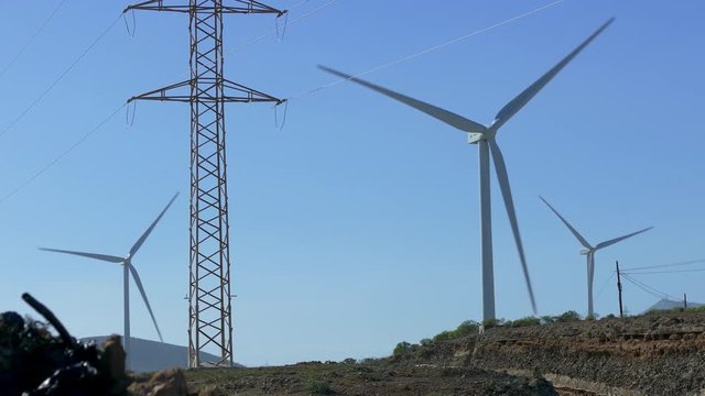 Wind turbines with rotating blades next to electrical towers and power poles on Tenerife, Canary Islands.