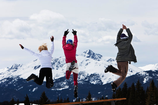 Three beautiful women having fun jump off a picnic table in Vail, Colorado.