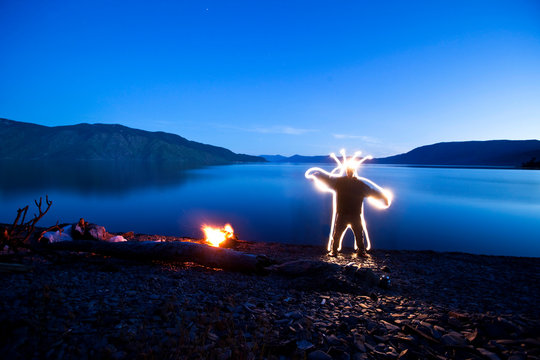 A creature stands next to a campfire and lake in Sandpoint, Idaho. This light painting image was created with a long exposure and flash lights.