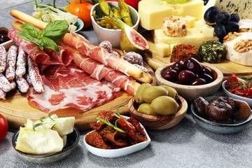 Italian antipasti wine snacks set. Cheese variety, Mediterranean olives, crudo, Prosciutto di Parma, salami and wine in glasses over grunge background.