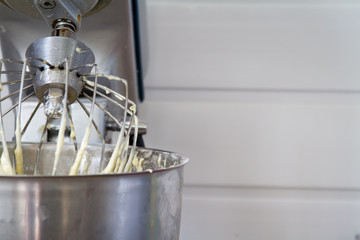 Closeup of electric mixer with whipped smooth dough for cake. Batter being whipped. Mixing white dough in bowl with motor mixer.