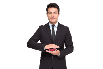 Portrait of a charming businessman dressed in suit holding toy car while standing isolated over...