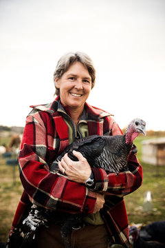 Portrait of smiling woman holding turkey on farm