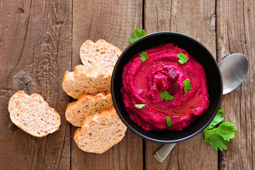 Beet hummus dip, overhead view table scene with bread on a rustic wood background