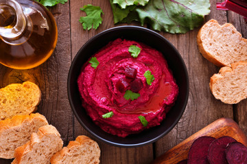 Beet hummus dip, overhead view table scene with bread and ingredients on a rustic wood background
