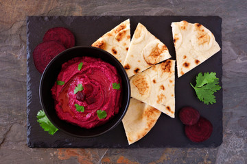 Beet hummus dip with pita bread on a slate platter, above view on a dark background