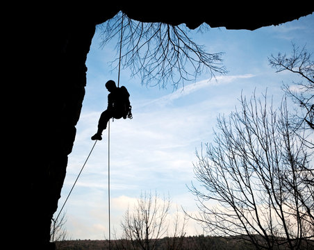 A climber rappels down from the side of a cliff (silhouette).