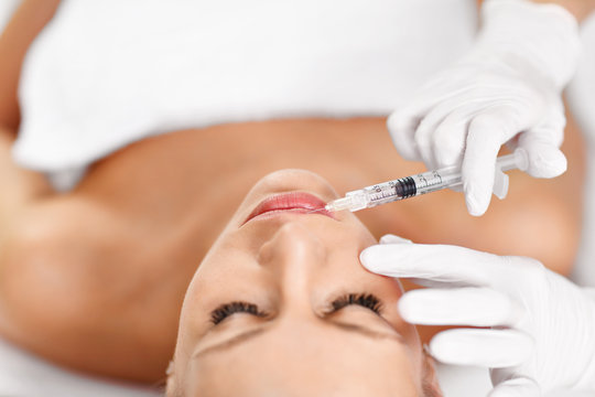 Close up of hands of cosmetologist making botox injection in female lips