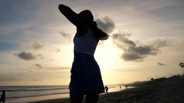 Young, happy woman dancing on beach during sunset, super slow motion