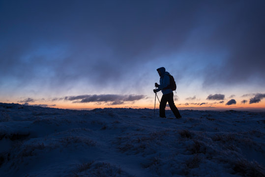 Silhouette of hiker on wintry summit of Corn Du at dawn, Brecon Beacons national park, Wales