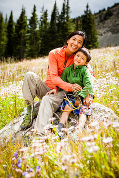 A mid-thirty year old Japanese-American mother sits wither her five year old son on a rock in a meadow of wild flowers on the way to Lower Crystal Lake, Colorado.