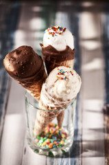 white and chocolate ice cream in a waffle glass with a colored pomace. Located in a glass on a wooden table