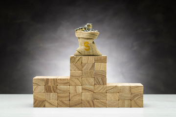 Concept of competition. Wooden podium on grey background with bag full of coins.