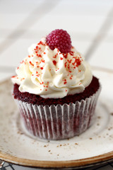 Homemade bakery style red velvet delicious sponge cupcake with white butter cream frosting and on raspberrie top on plate. Candy bar for celebrating partys and birthdays